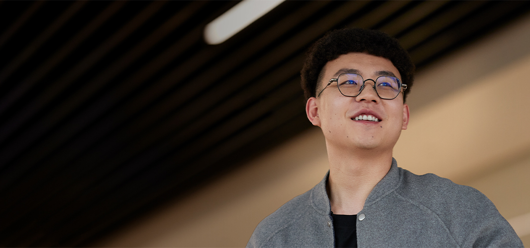 Jason de pie dentro de un edificio, sonriendo y mirando hacia la derecha.