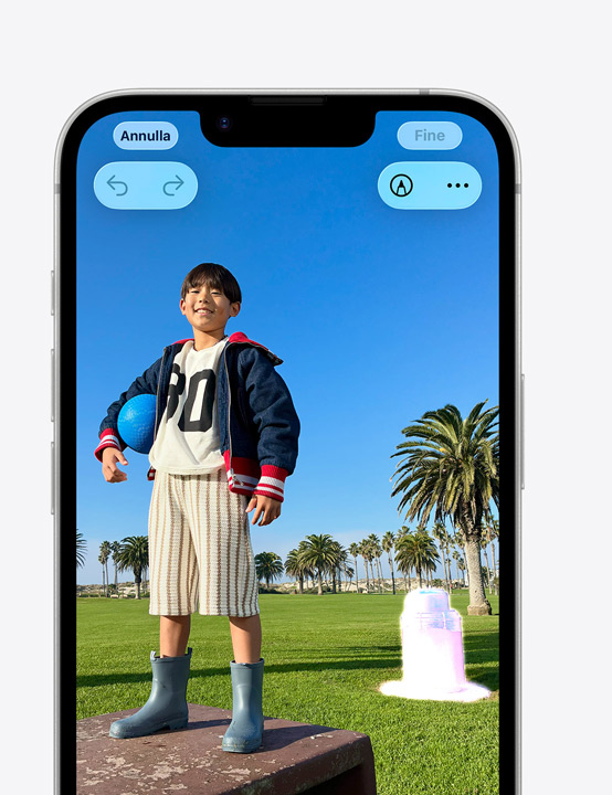 iPhone che mostra la foto di una persona sorridente in un parco, e l’uso dello strumento Ripulisci per rimuovere un cestino della spazzatura sullo sfondo