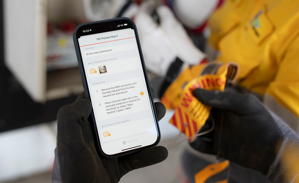 作業人員手持 iPhone，螢幕上顯示著執行配電盤測試的說明，以及 13C Process Step 3 的字樣