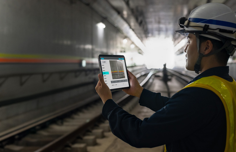 Un membre de l’équipe d’entretien des tunnels de Tokyo Metro tient un iPad pour photographier les voies, accompagné d’une personne de son équipe qui l’observe.