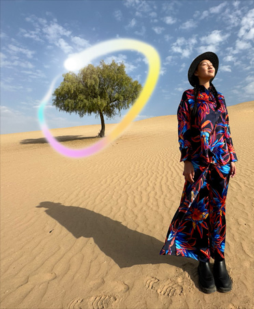 Photo d’une femme en robe multicolore debout dans un paysage désertique avec un arbre derrière elle entouré d’un dégradé arc-en-ciel lumineux montrant la capacité d’Apple Intelligence à effacer les objets en arrière-plan
