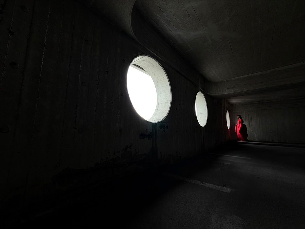 Una mujer con vestido largo rojo está siendo fotografiada de pie en una sala vacía. La distancia focal de la imagen avanza en la app Fotos para demostrar las capacidades del sistema de cámaras Pro, se muestra una distancia focal de 13 mm
