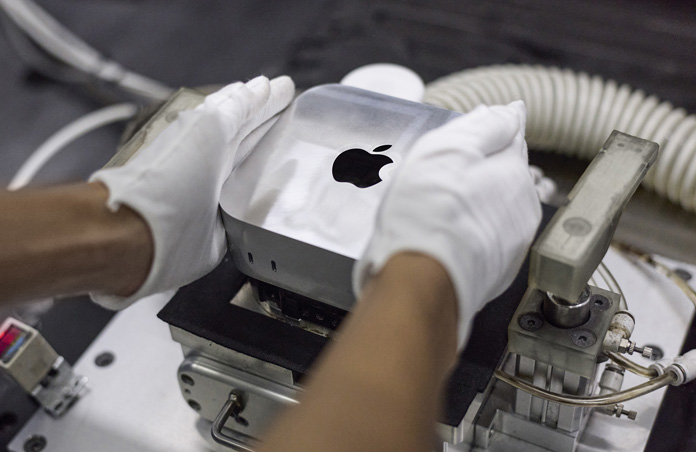 Gloved hands placing a Mac mini into a manufacturing machine during assembly