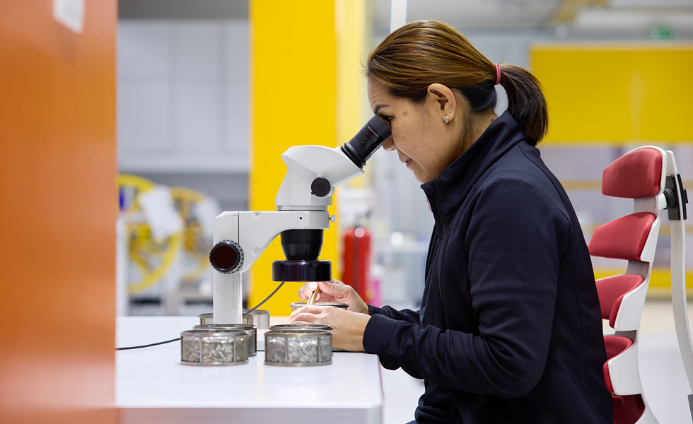 An technician inspects assembly components through a stereo scope